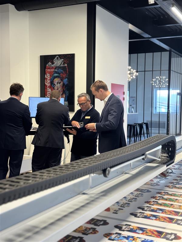 Échange entre visiteurs et partenaire devant une impression en cours